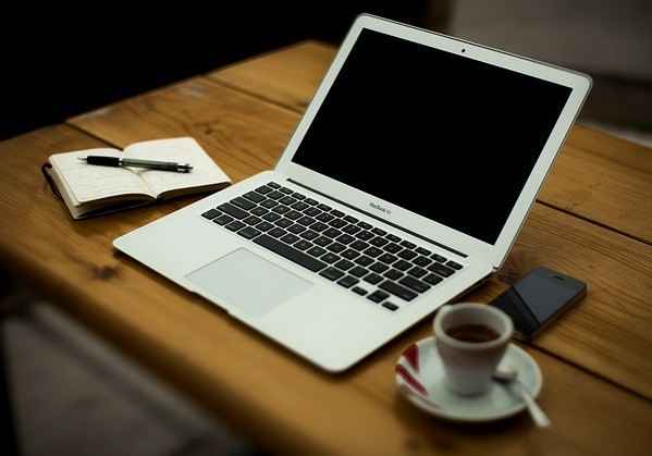 Open laptop computer on a desk with a cup of coffee and a pad with a pen on it.